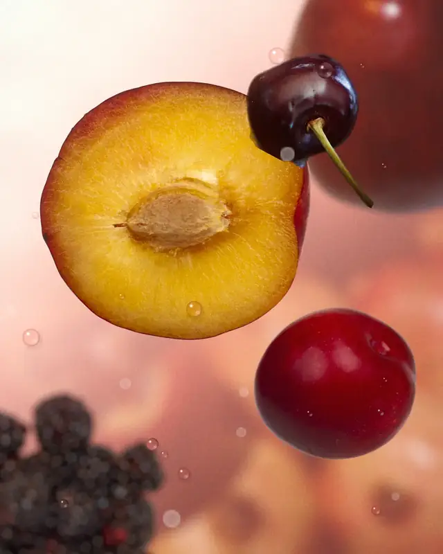 Planche : une prune coupée en deux, des cerises, des mûres et des gouttes de jus en suspension